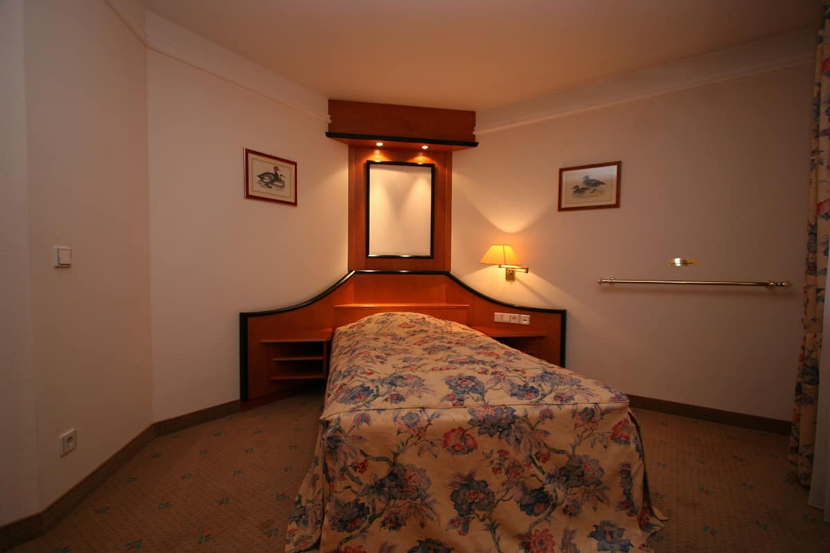 A hotel room with a bed, a nightstand, a mirror, and a wall-mounted lamp.