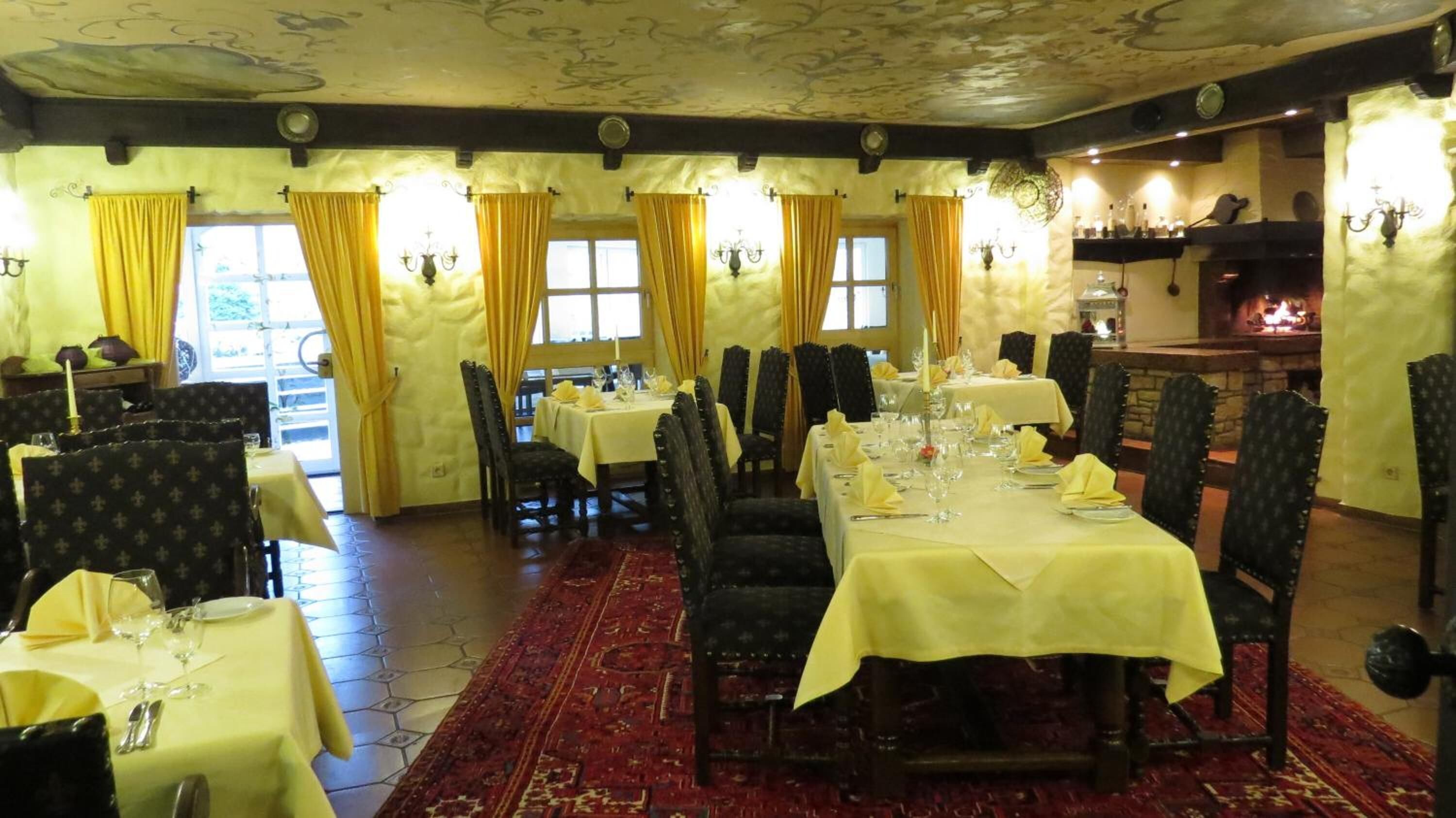 Une salle à manger avec des tables dressées, un sol à motifs et une cheminée en arrière-plan.