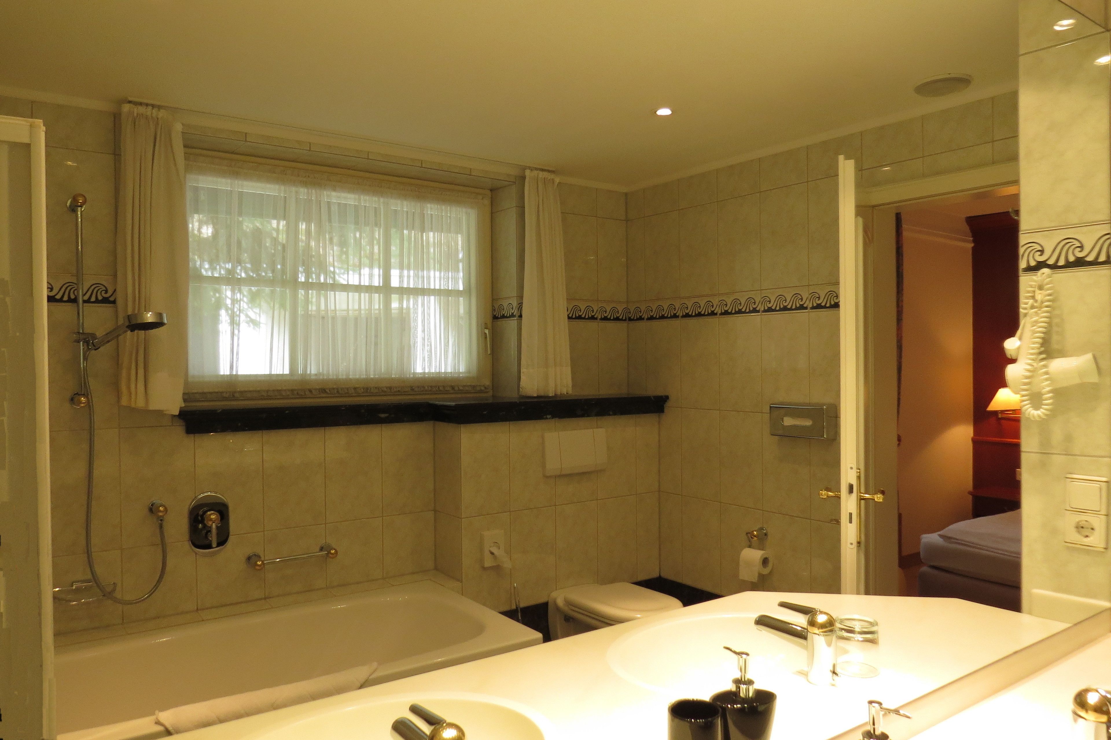 Un bagno con vasca, due lavandini, un water e una finestra con tende.