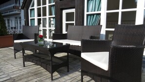 Mobilier d’extérieur en osier, agrémenté de coussins et accompagné d’une table en verre, installé sur une terrasse carrelée.