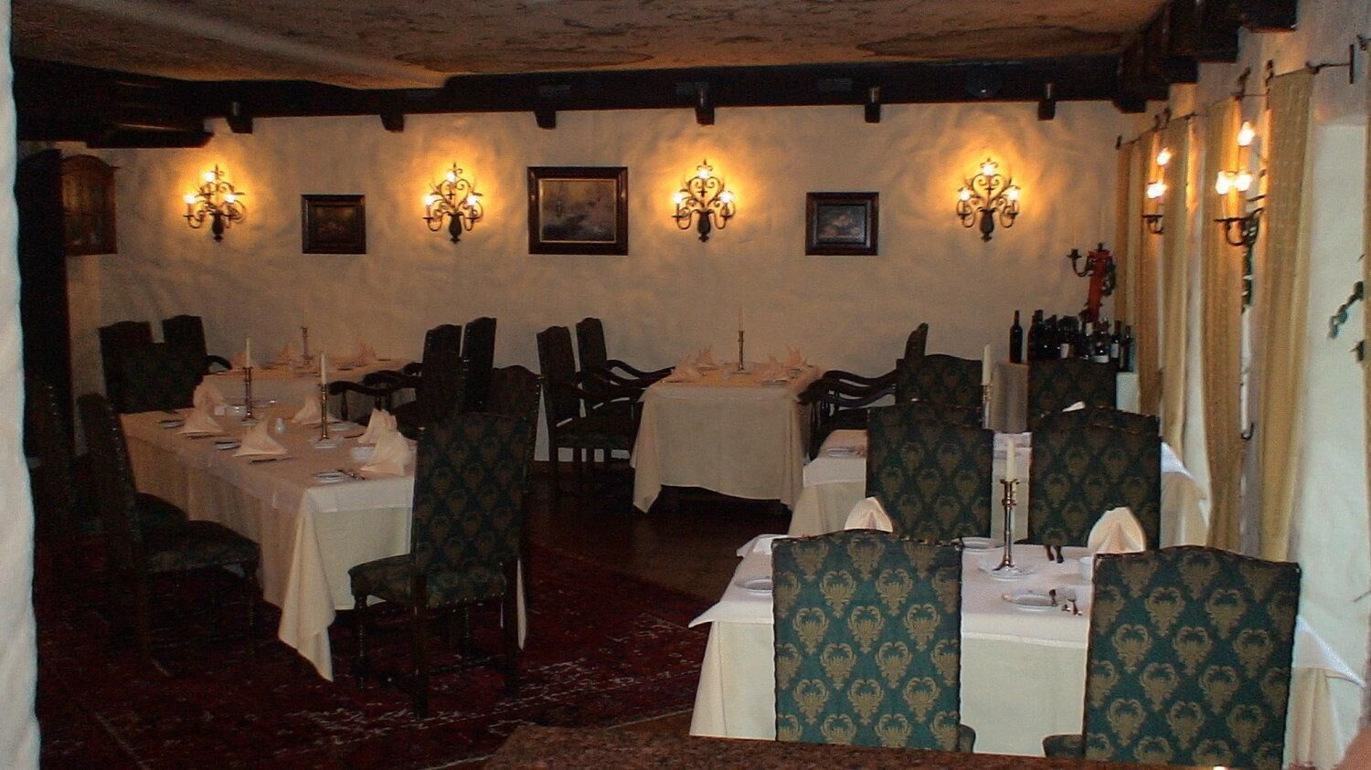 Un espace repas avec des tables dressées, des lustres fixés au mur et des œuvres d’art encadrées qui décorent les murs.