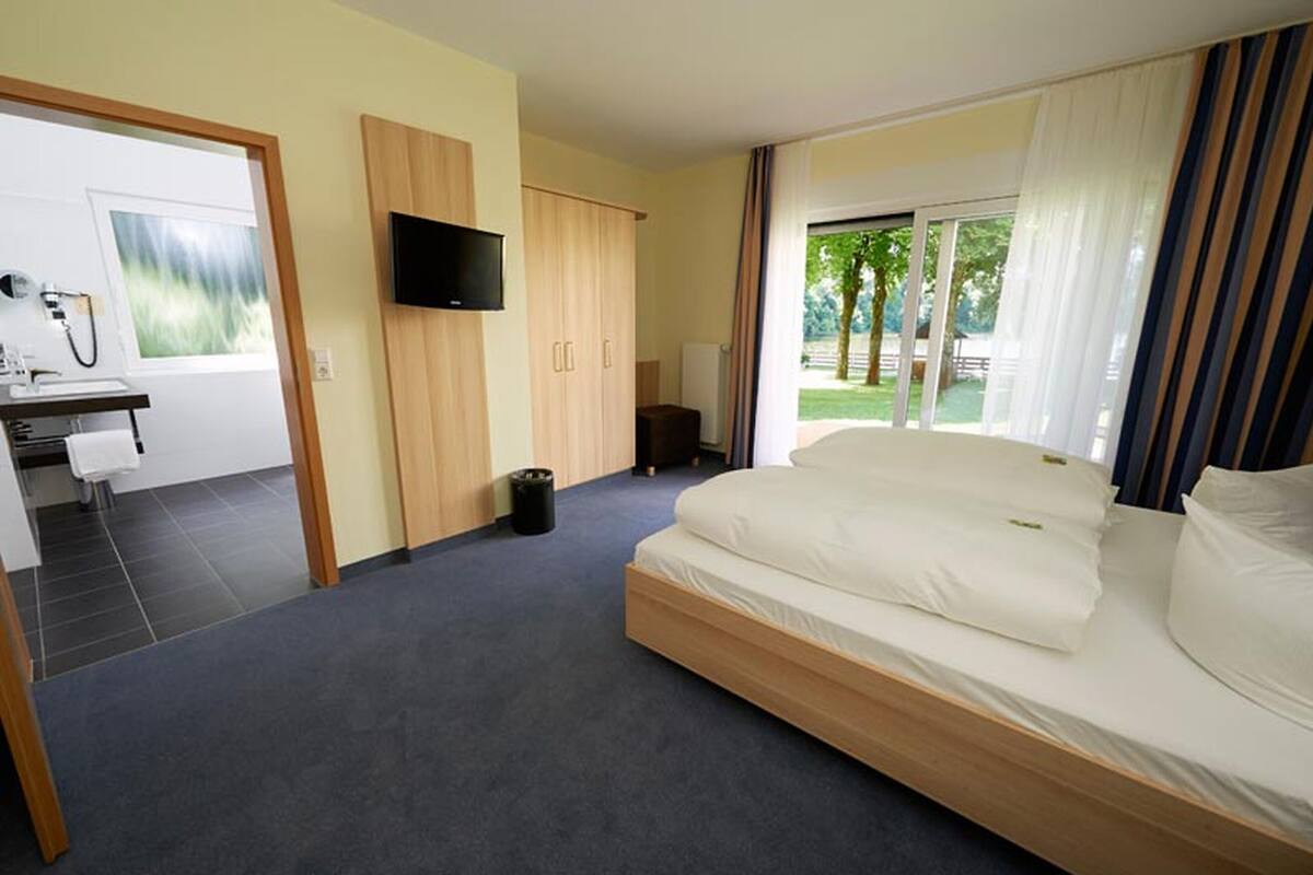 Habitación de hotel con cama, escritorio, silla, televisor y vista al exterior.