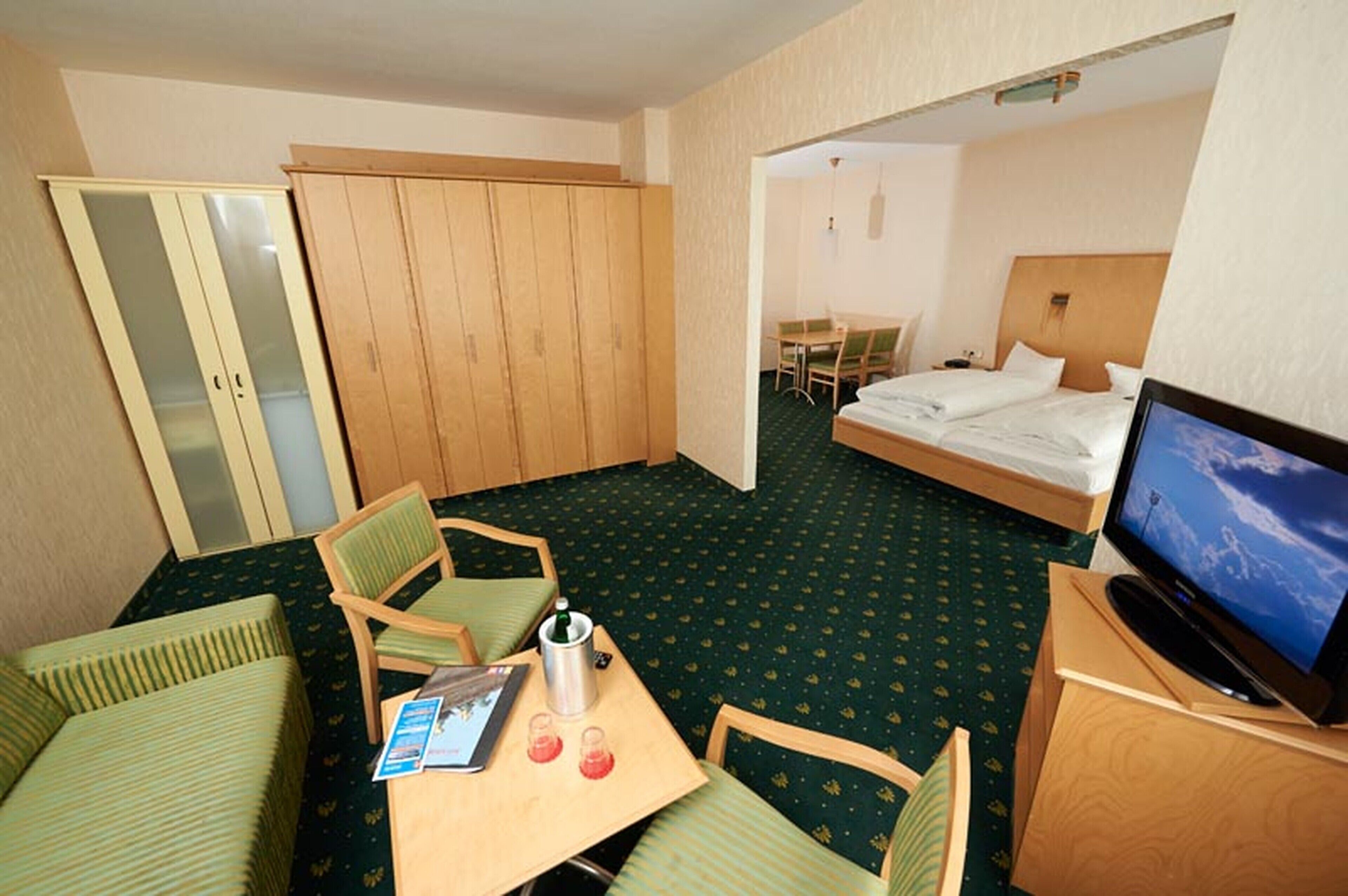 Habitació d'hotel amb llit, televisió, escriptori amb cadira, taula petita i armari.