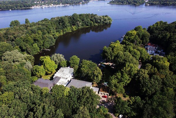 An aerial view of a lakeside property with dense forestation, a small dock, and a few buildings. - Seehotel Grunewald (Berlin)