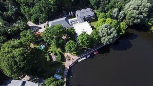 Vista aérea de una propiedad frente al lago con un muelle, una casa grande y árboles densos alrededor.