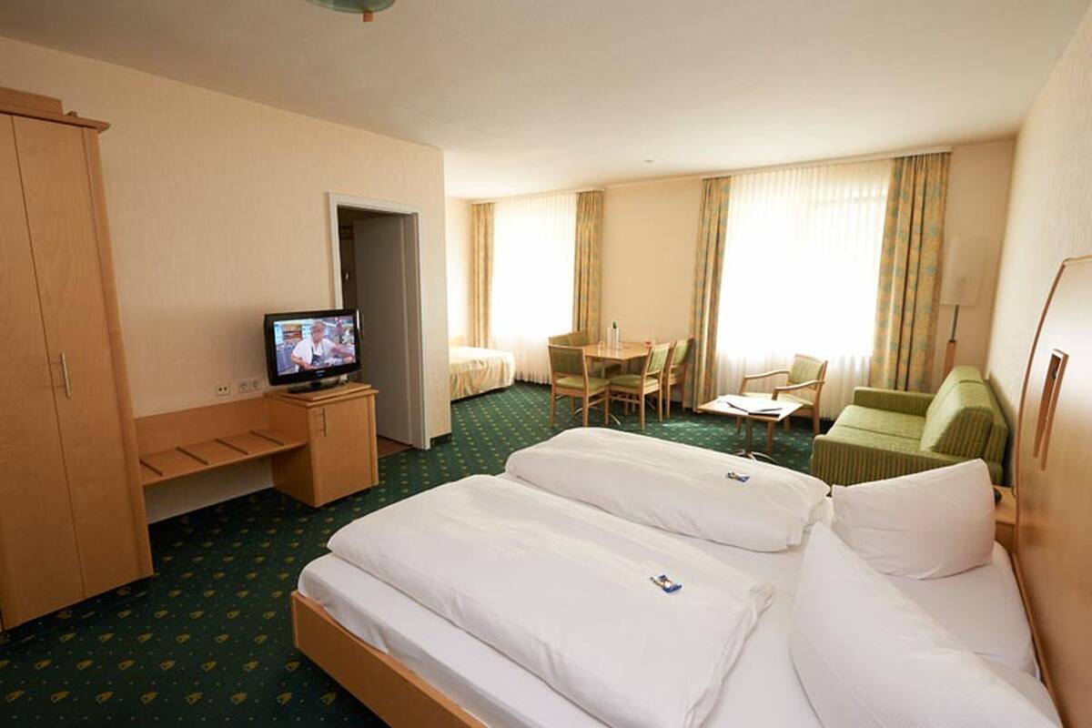 Quarto de hotel com duas camas, uma escrivaninha, televisão e área de refeições.