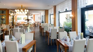 Un restaurante espacioso con techos altos, candelabros modernos y vistas al área de mesas al aire libre.