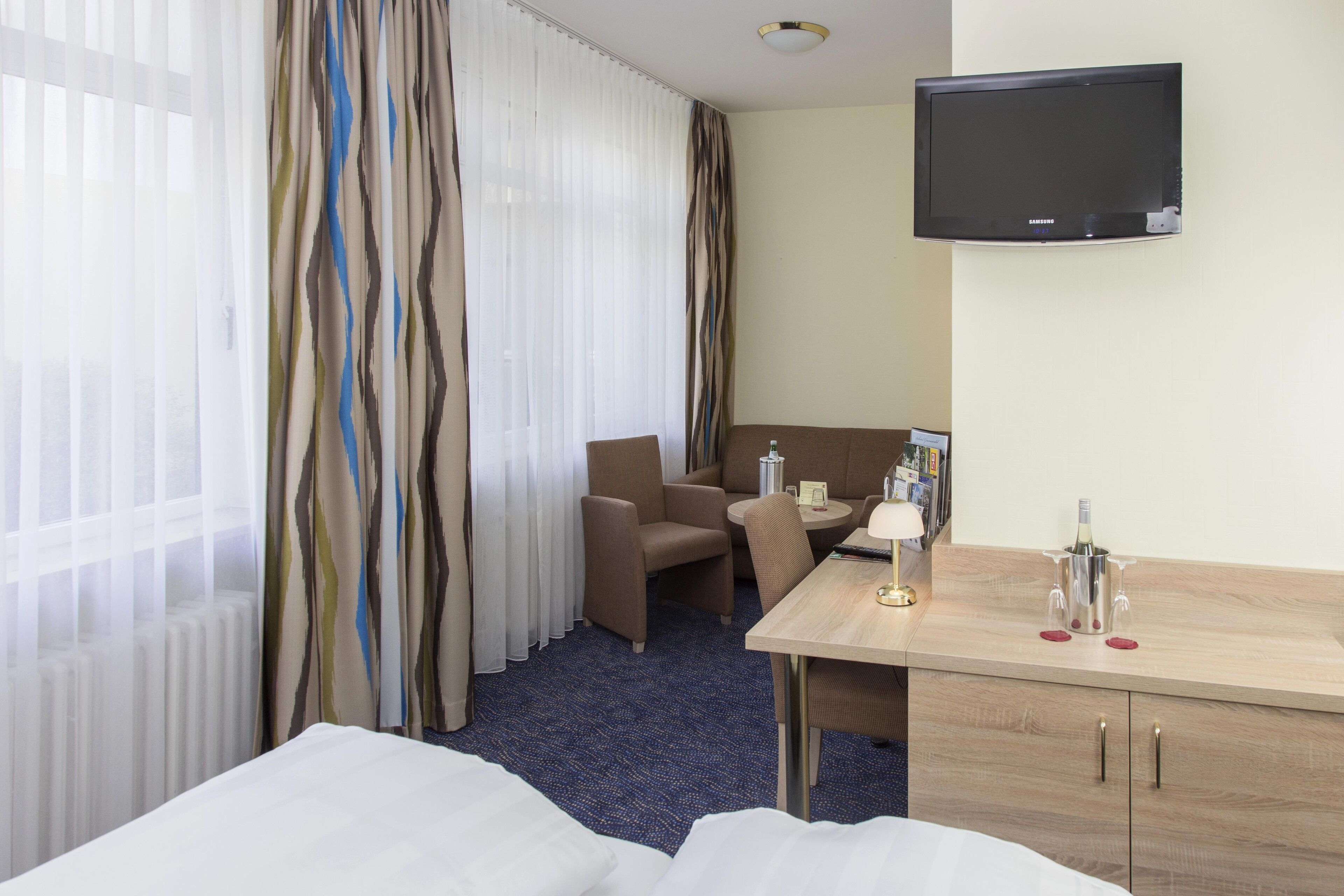 A hotel room with a bed, a desk, a chair, a television, and a minibar.