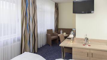 A hotel room with a bed, a desk, a chair, a television, and a minibar.