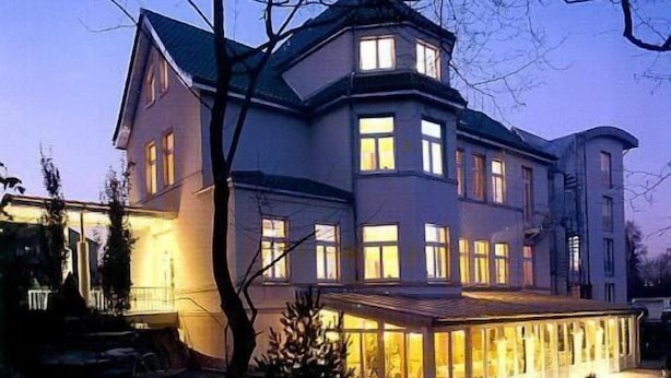 A large, multi-story building with a prominent corner tower and a covered outdoor area with glass walls. - Hotel Das Lola (Essen)