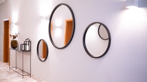A hallway with three wall-mounted mirrors, a marble floor, and a small table with a vase and decorative items. - Hotel Das Lola (Essen)