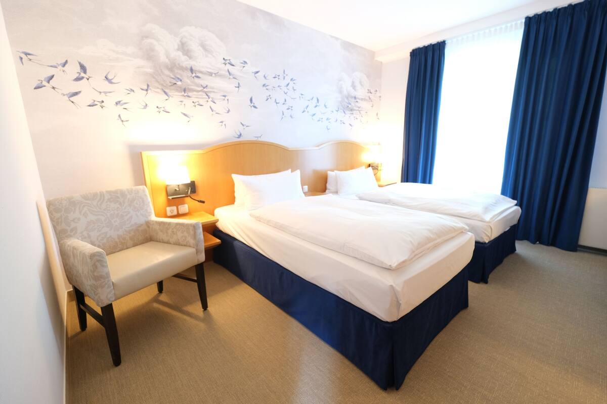 A hotel room with a large bed, a chair, a nightstand with a lamp, and a wall mural.