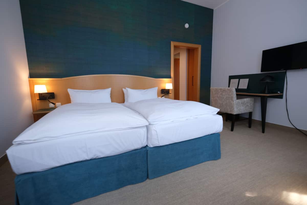 A hotel room with a large bed, two bedside tables with lamps, a desk with a chair, and a flat-screen TV mounted on the wall.