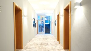 A hallway with marble flooring, wooden doors, and wall-mounted light fixtures. - Hotel Das Lola (Essen)