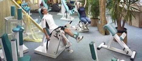 A gym with various exercise machines and a few people working out.
