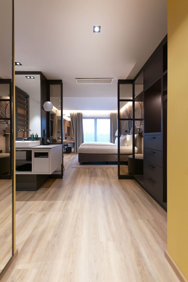 Una habitación de hotel moderna con una cama grande, un escritorio con espejo, un armario y un área de baño.