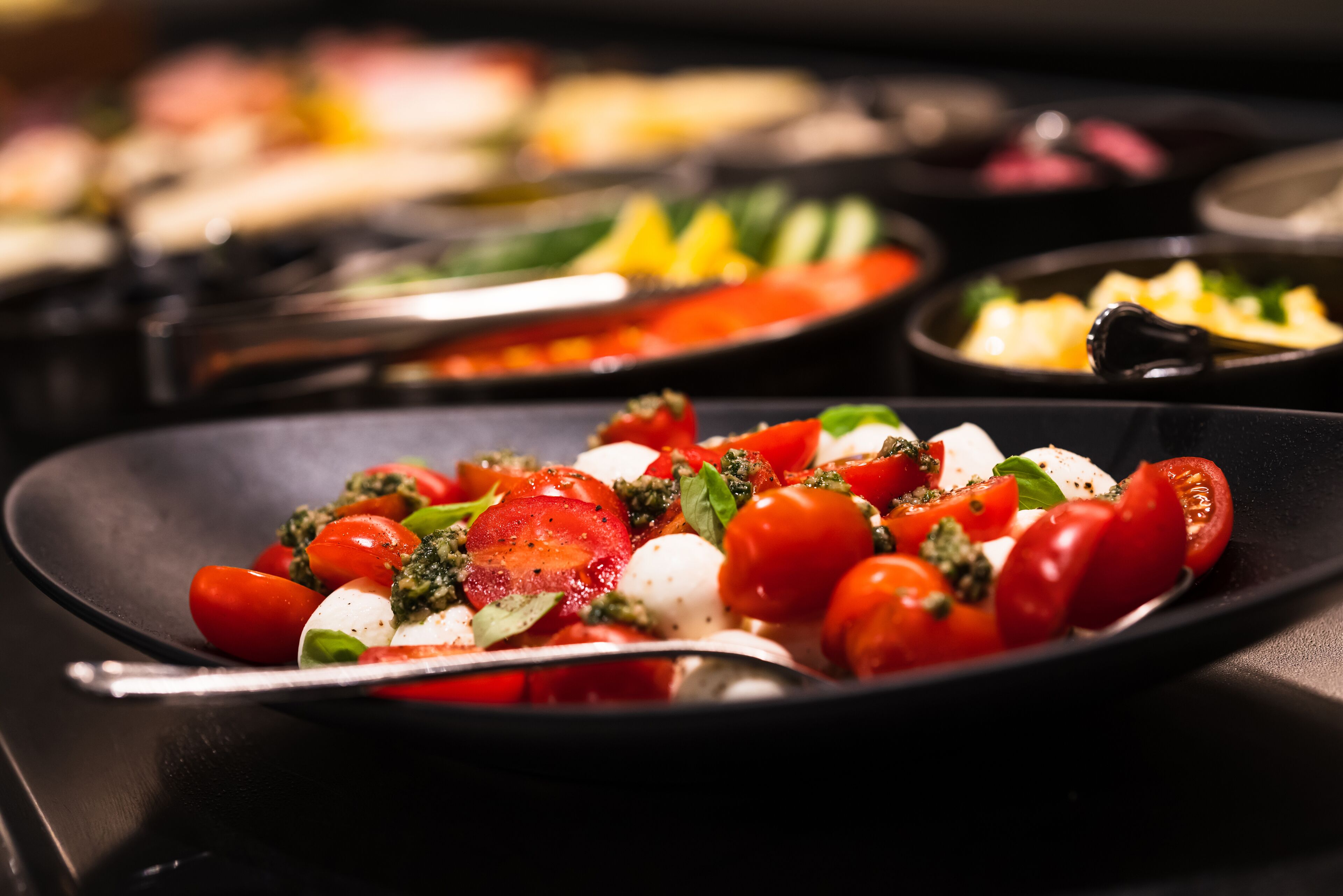 Primer plano de un plato con tomates, mozzarella y albahaca sobre una fuente negra.