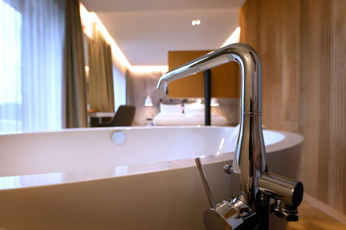 A modern bathroom with a large bathtub, a sleek chrome faucet, and a mirror reflecting the room.