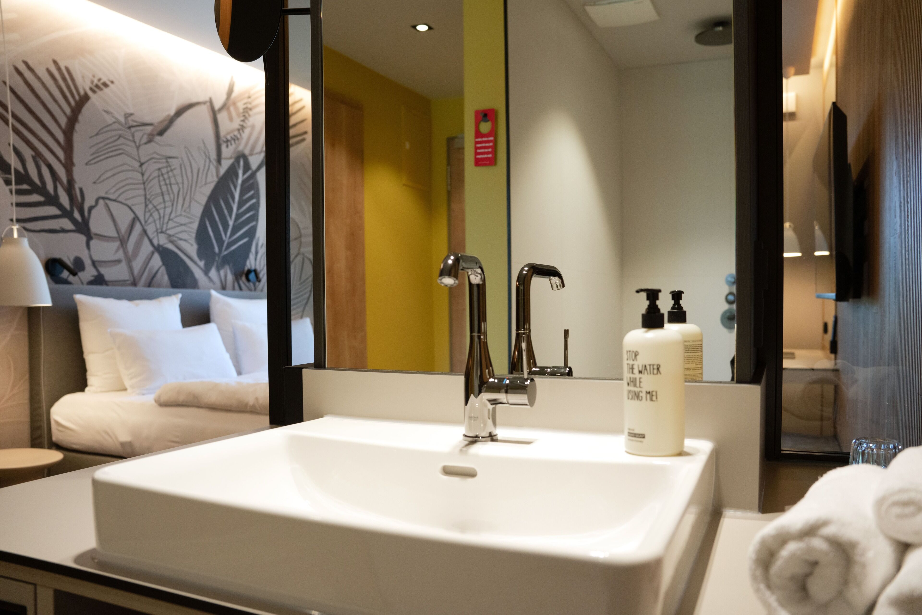 A hotel bathroom with a white sink, a mirror, and a towel rack.