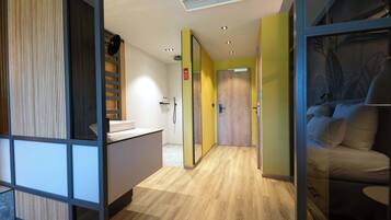 A hotel corridor with wooden flooring, a reception area, and a bed with a headboard.