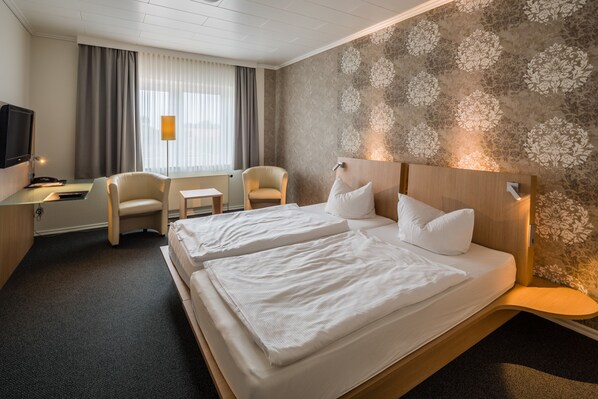 A hotel room with two beds, a desk with a computer, a chair, and a TV. - Thöles Hotel Bücken (Bücken)