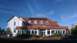 Un bâtiment à deux étages, doté d’un toit recouvert de tuiles rouges et d’une enseigne indiquant qu’il s’agit d’un hôtel et d’un restaurant.