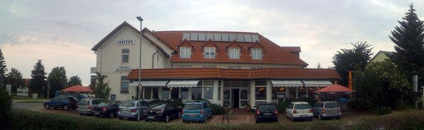 A two-story building with a sign indicating it is a hotel and restaurant. There are multiple cars parked in front, and the building has a red-tiled roof. - Hotel Kiebitz an der Ostsee (Boergerende-Rethwisch)