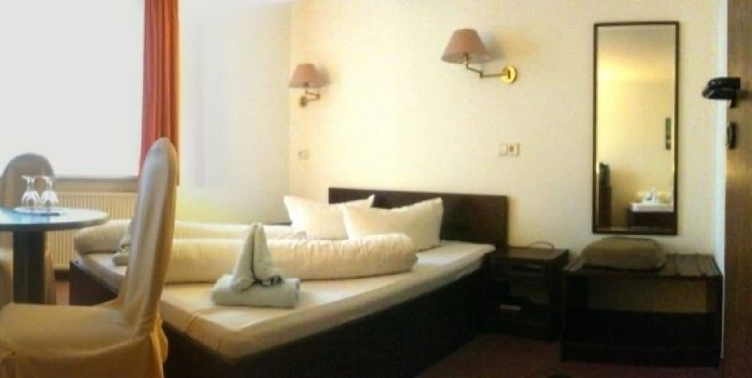 A hotel room with a bed, a chair, a table, a lamp, and a mirror.