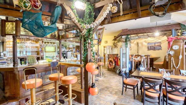 Un coin bar au style rustique, avec des poutres en bois, un comptoir, des tabourets et des décorations suspendues.