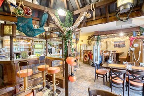 Un coin bar au style rustique, avec des poutres en bois, un comptoir, des tabourets et des décorations suspendues.