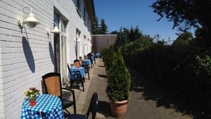 Un espace extérieur aménagé avec des tables et des chaises, un pot de fleurs et un bâtiment à la façade de couleur claire.