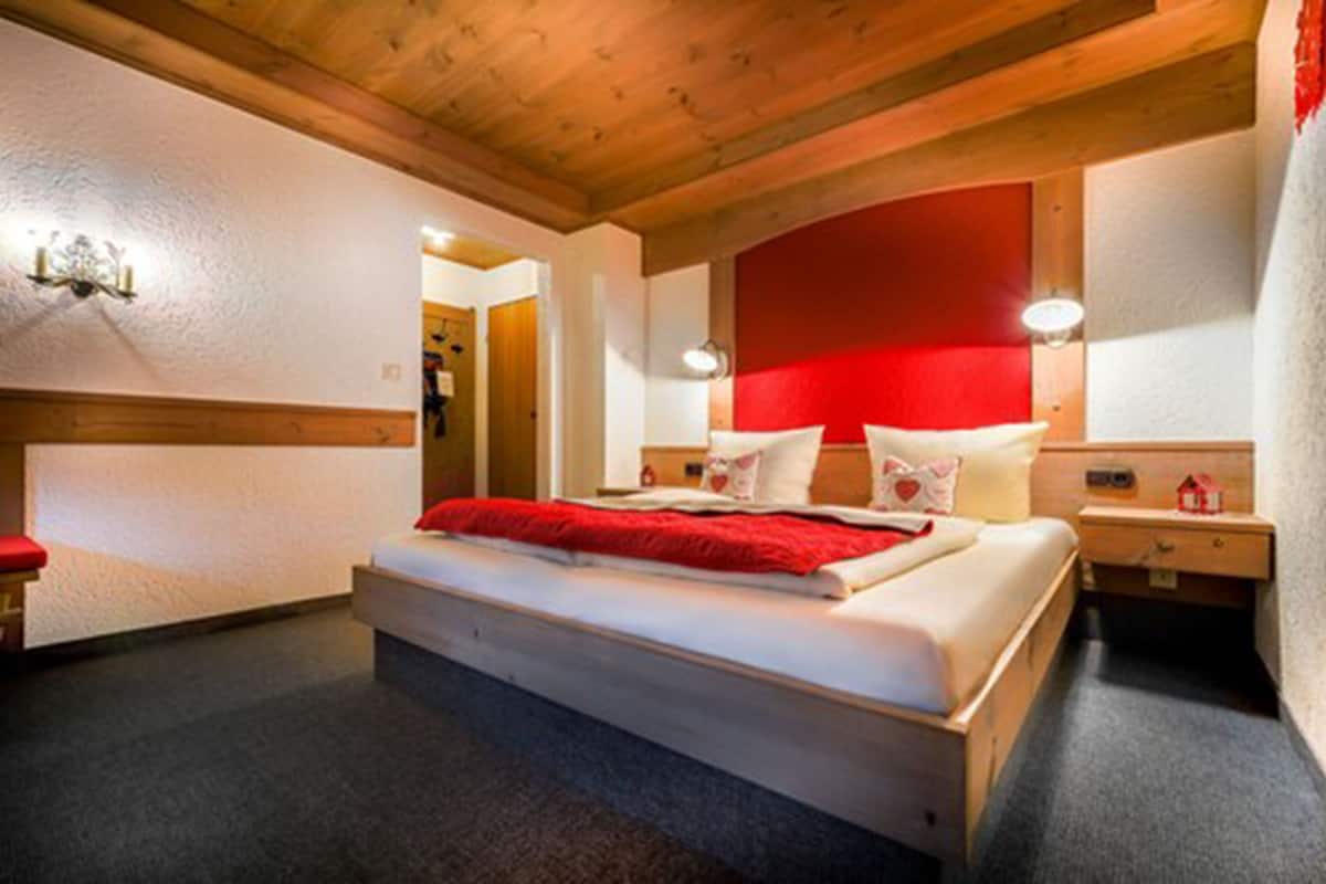 Un dormitorio con techo de madera, una pared de acento roja, una cama con ropa de cama blanca y mesitas de noche con lámparas.