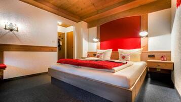 Camera da letto con soffitto in legno, parete di accentazione rossa, letto con biancheria bianca e comodini con lampade.