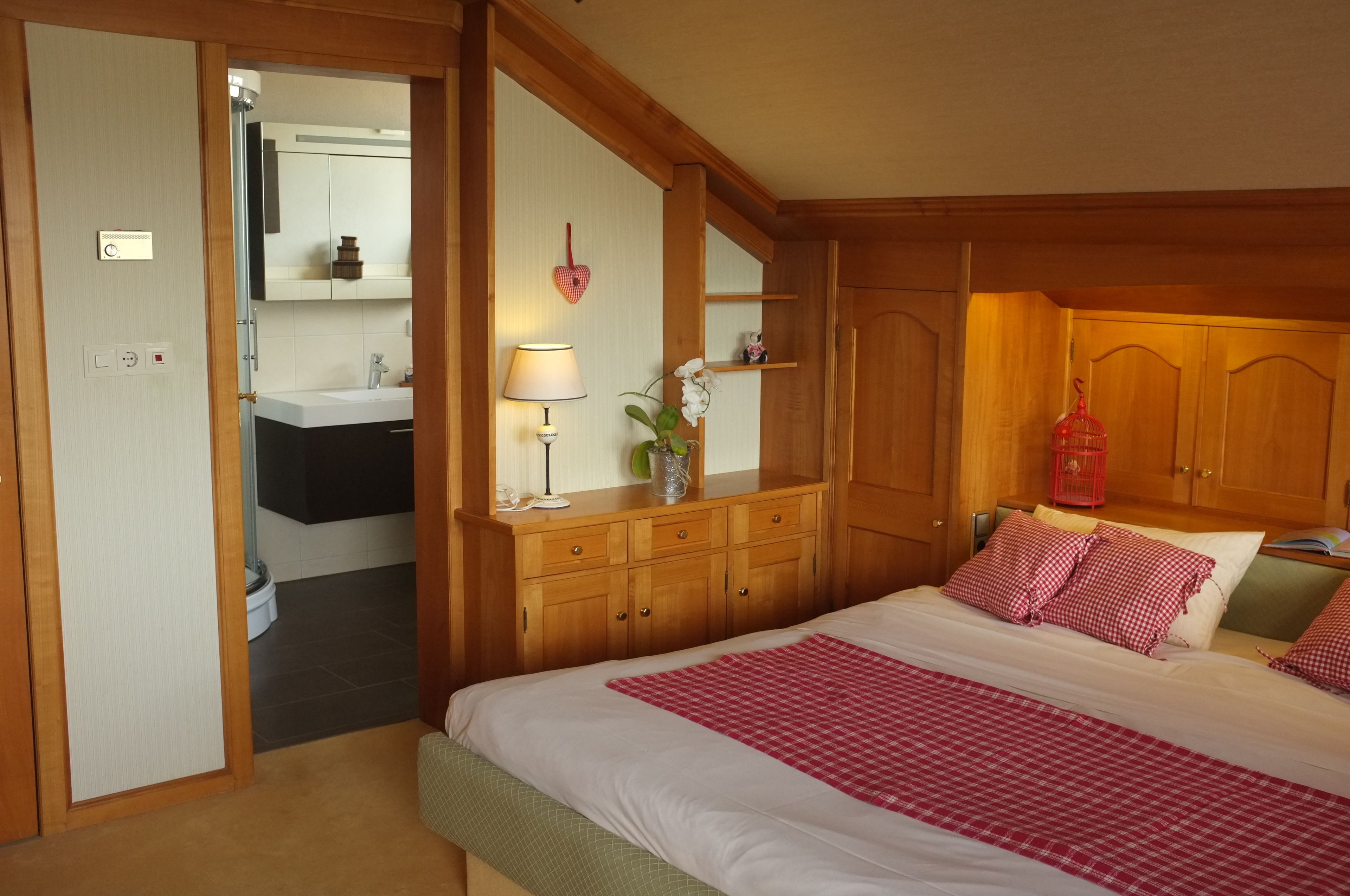 Un dormitorio con cama, armario de madera, mesita de noche, lámpara y una pequeña planta en maceta.