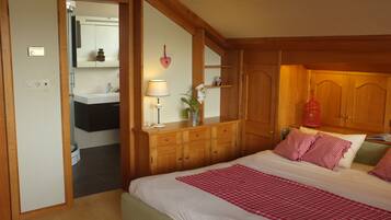 Un dormitorio con cama, armario de madera, mesita de noche, lámpara y una pequeña planta en maceta.