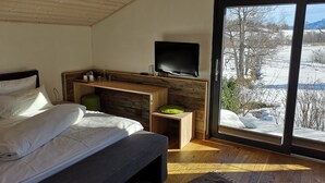 Un dormitorio con cama, televisor, escritorio de madera y un ventanal con vista a un paisaje nevado.