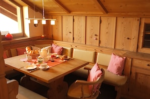 A wooden dining area with a table set for two, benches with red and white checkered cushions, and a wooden cabinet with a window above.