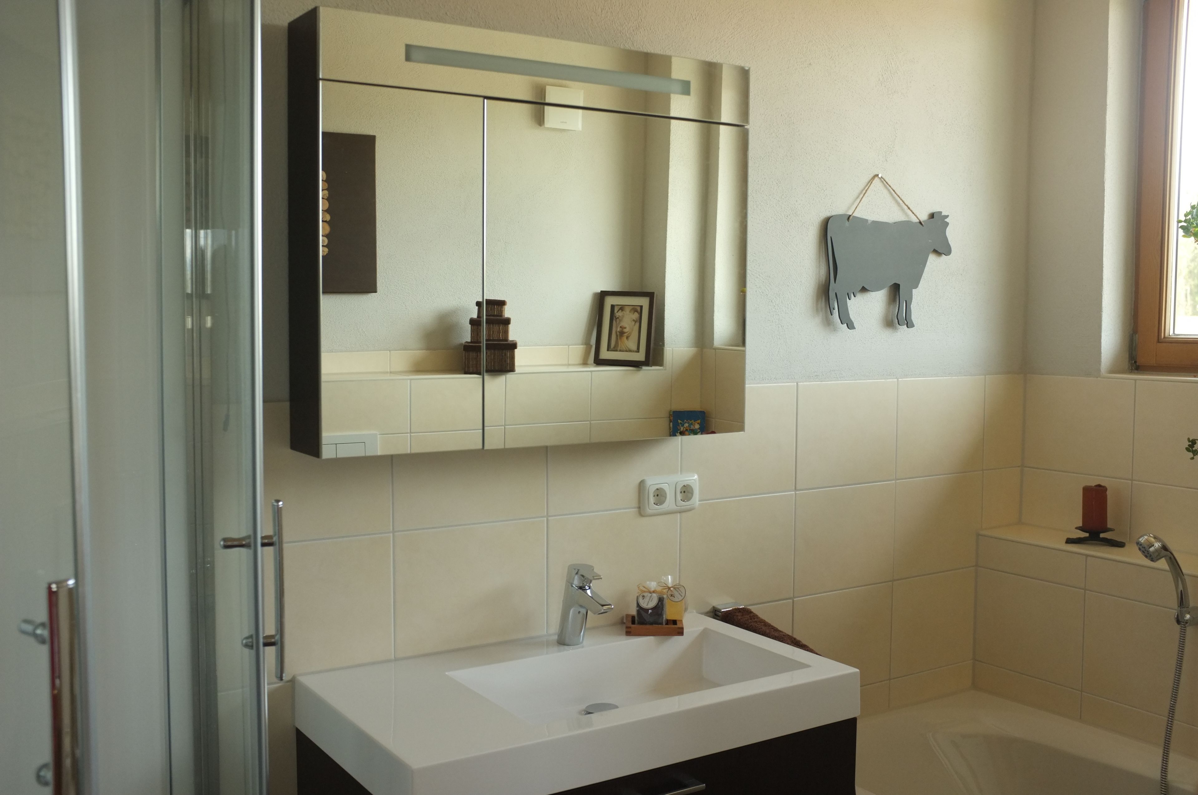 A bathroom with a large mirror, a sink, a shower, and a cow decoration on the wall.