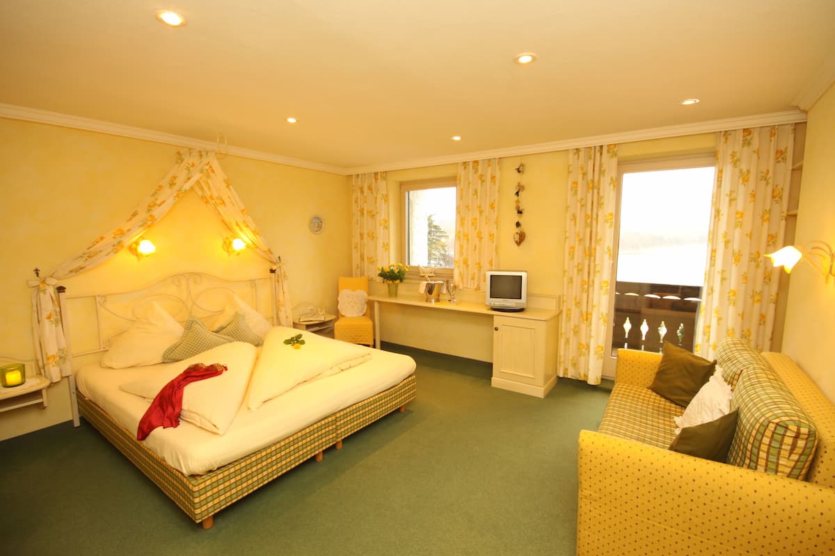 Una habitación de hotel con cama, sofá, escritorio con televisor y ventana con cortinas.