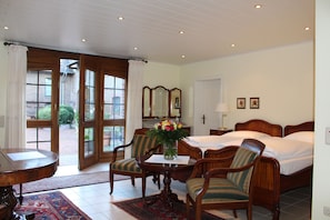 A hotel room with a bed, two chairs, a table with a vase of flowers, a desk, and a window with curtains. - Landhaus Göddertzhof (Erkelenz)