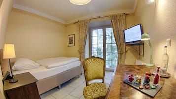 Una habitación de hotel con cama, sillón, escritorio con lámpara, televisor y ventana con cortinas.