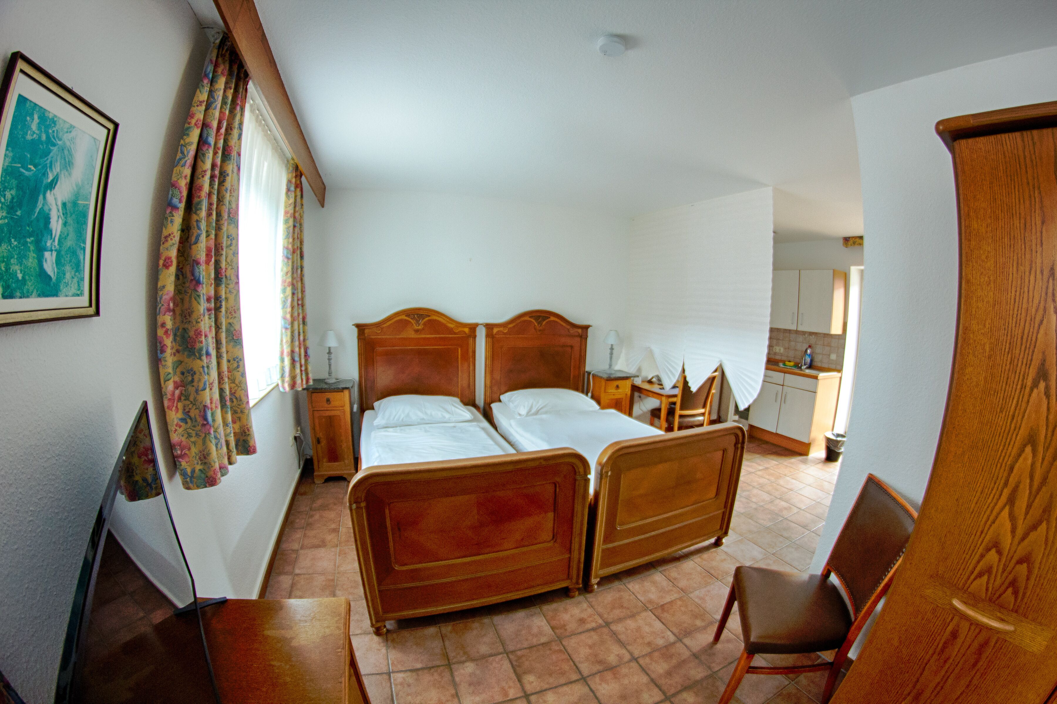 Quarto com duas camas de madeira, uma cadeira, uma escrivaninha e uma mesa pequena.