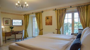 Habitación de hotel con una cama grande, un escritorio con silla, un televisor y una ventana con cortinas.