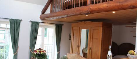 A spacious living room with a wooden staircase, a sofa, a table with a vase of flowers, and a basket of fruit.