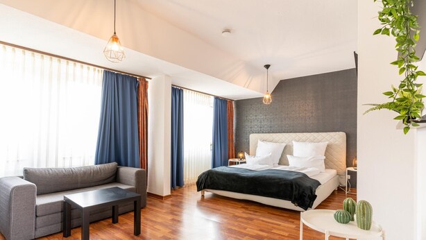 Ein modernes Hotelzimmer mit einem großen Bett, einer Sitzecke, einem kleinen Tisch und einem Blumentopf.