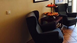 Ein Wohnzimmer mit zwei schwarzen Sesseln, einem kleinen Tisch mit Obstschale und gerahmten Kunstwerken an den Wänden.
