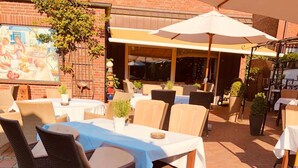 Eine Terrasse im Freien mit Korbmöbeln, einem Tisch mit weißer Tischdecke und Topfpflanzen.