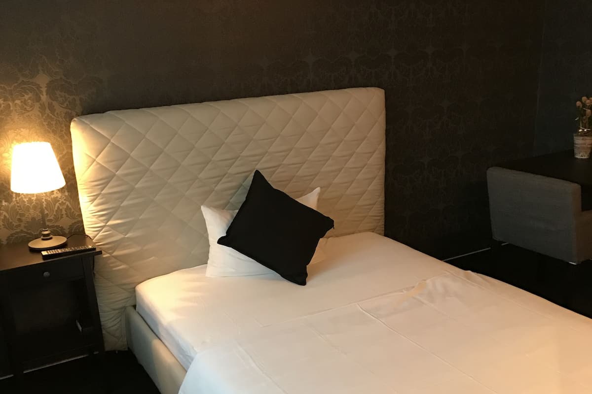 A neatly made bed with a quilted headboard, a bedside lamp, and a small table with a vase of flowers.