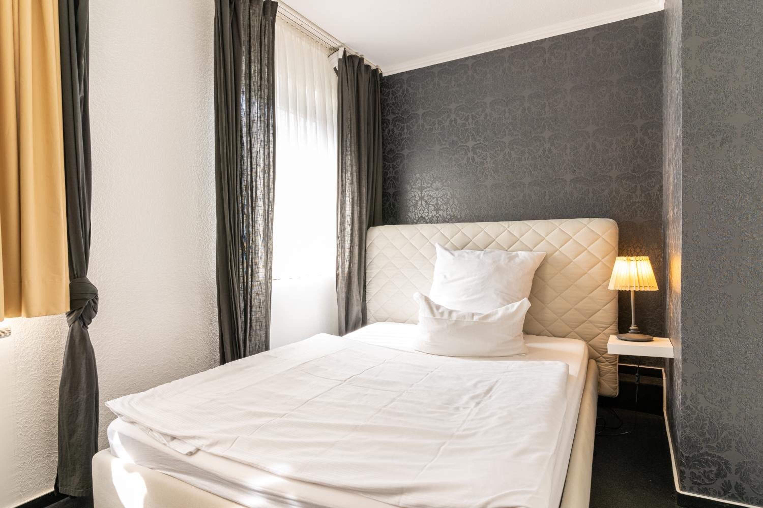 A neatly made bed with a quilted headboard, a bedside lamp, and a wall with a subtle pattern.