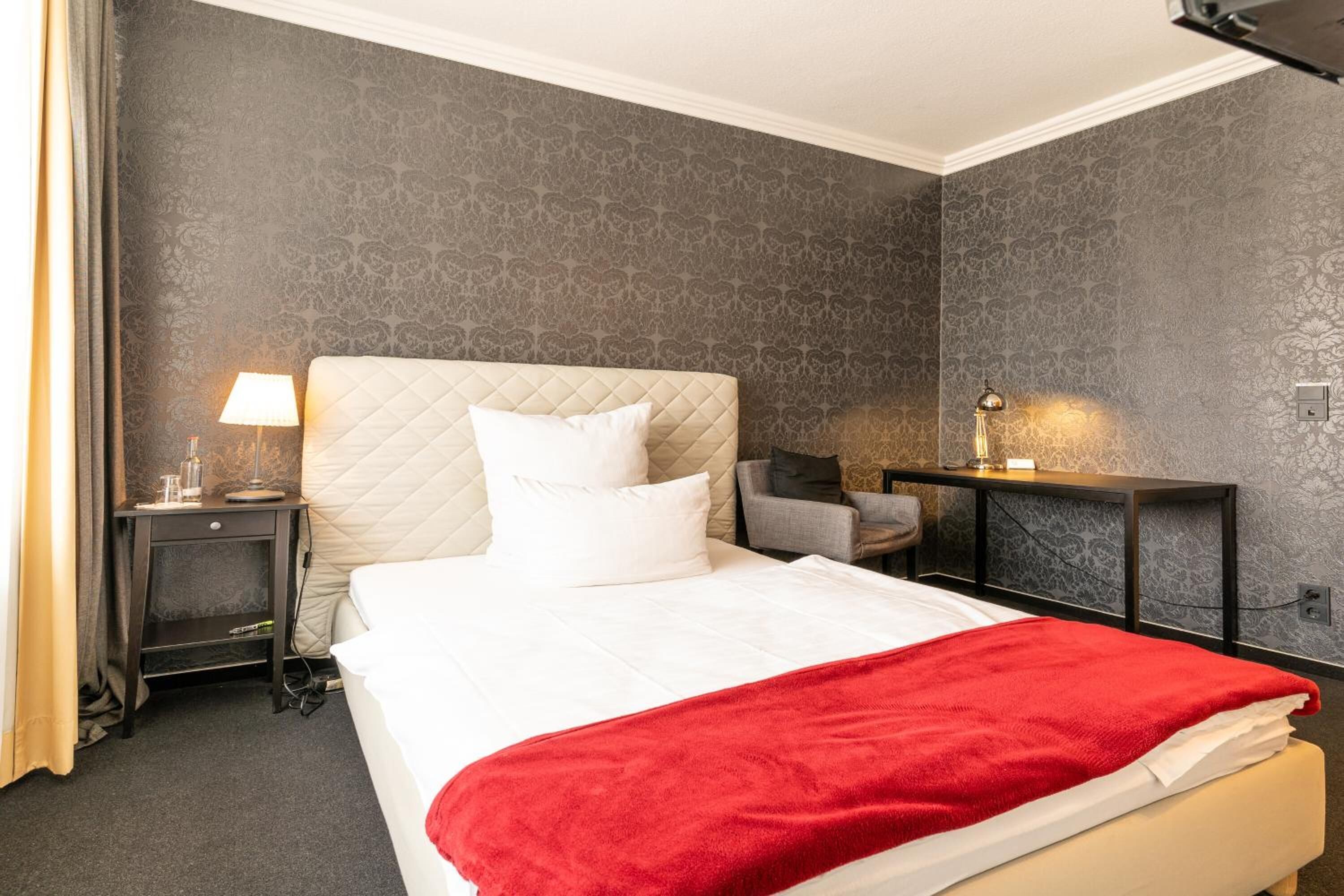 Une chambre d’hôtel avec un lit, une table de chevet, un bureau et une chaise.